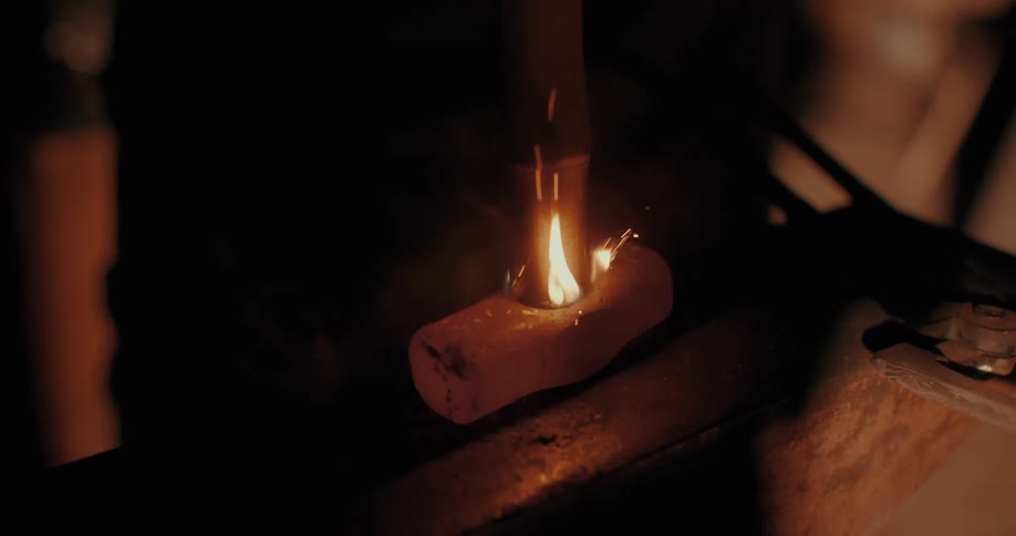 Sparks fly as a blacksmith inserts a handle into a red hot hammer head over an anvil