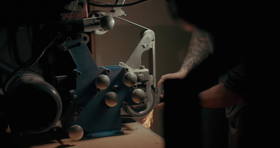 A person works on a metal grinding machine sparks flying as they shape the metal