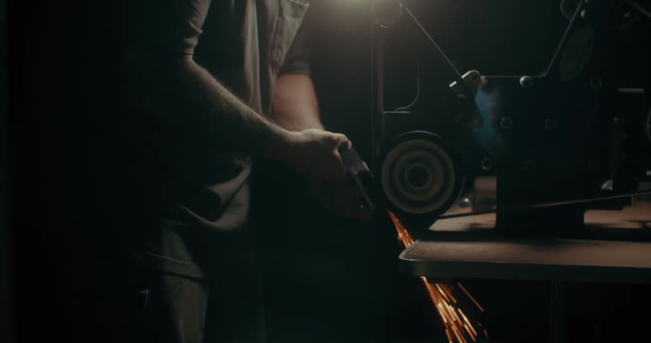 A man uses a machine to work on a piece of metal in a dark workshop