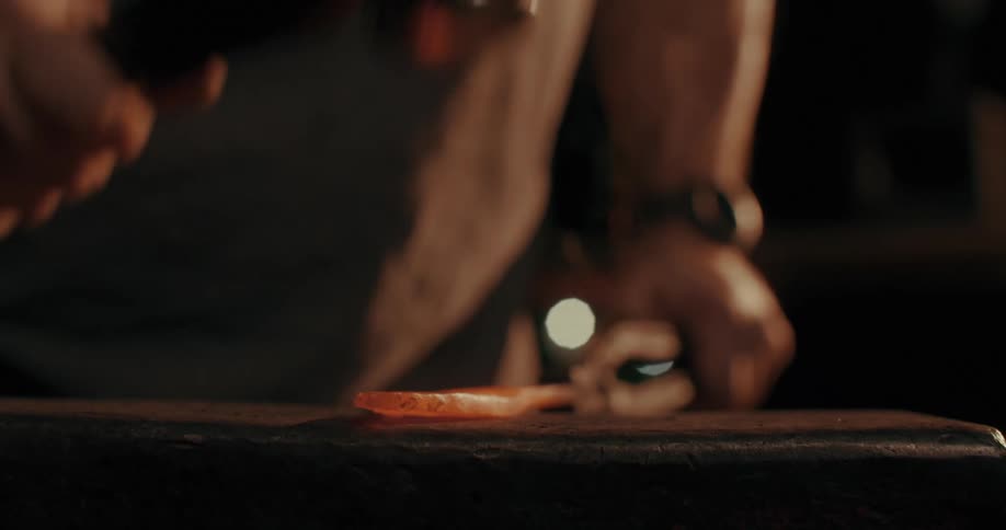 Closeup of a blacksmith hammering a hot piece of metal on an anvil