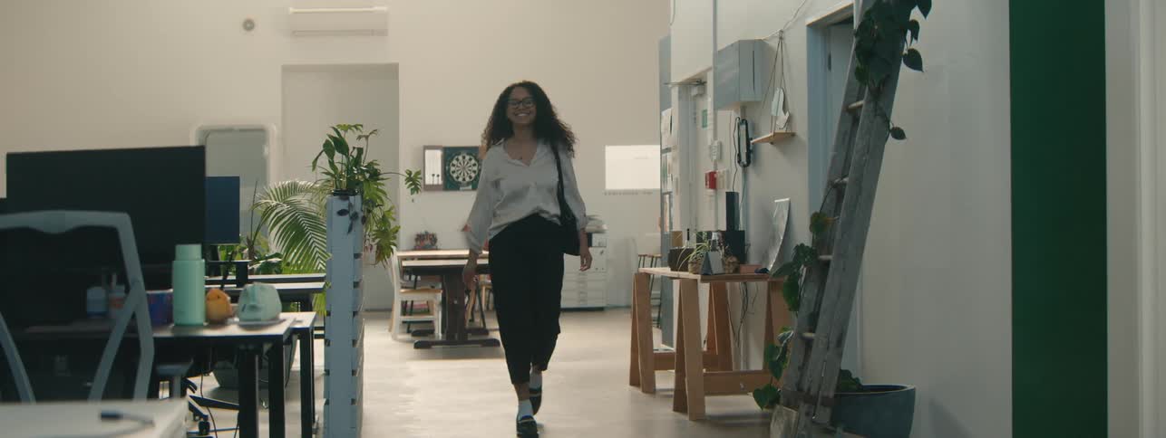 A young woman with curly hair walks through a modern office