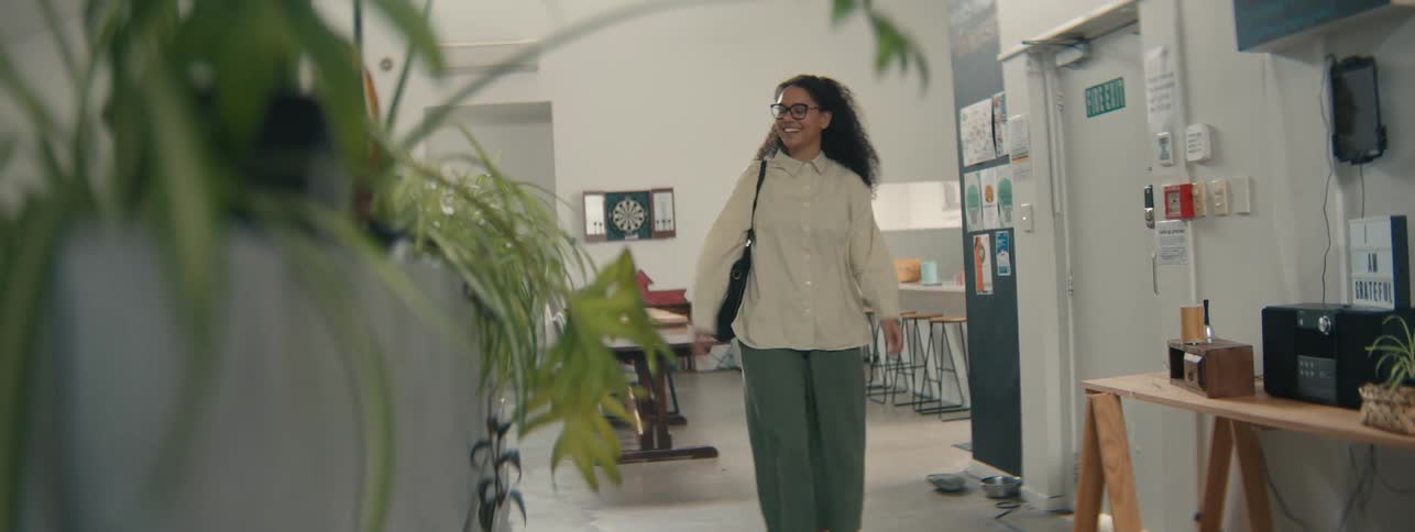 A happy young woman with curly hair walks down a modern office