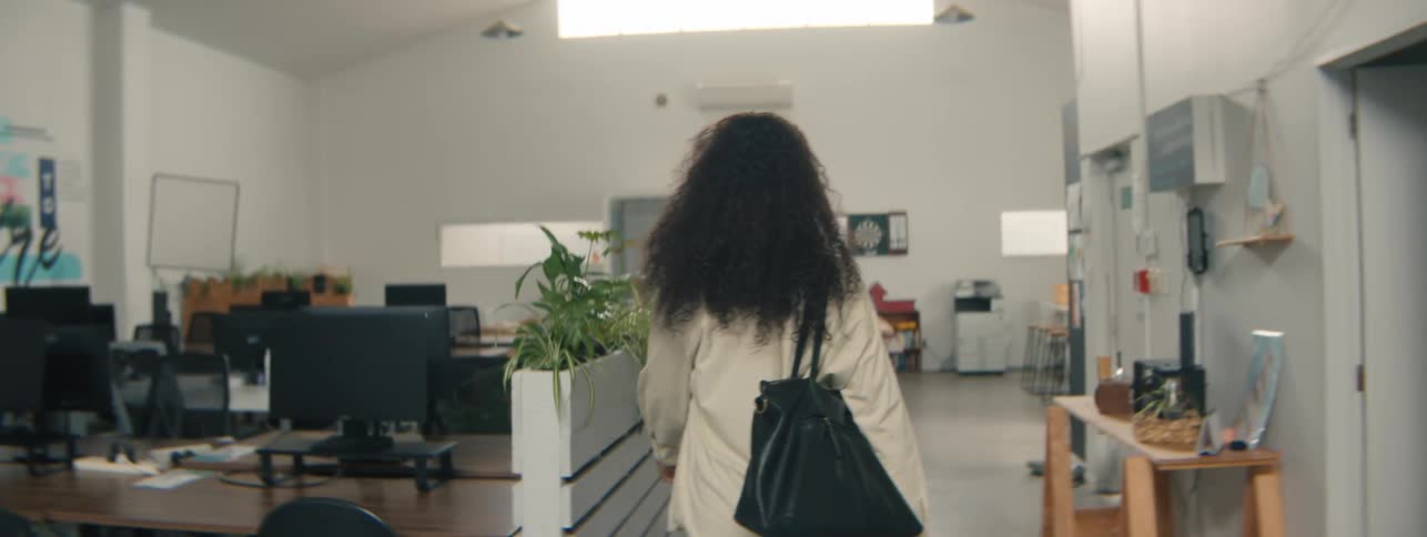 A young woman with curly hair walking through a modern office