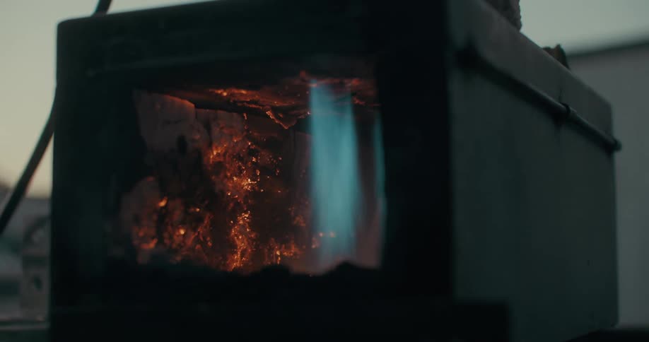 A small forge or furnace ignites with blue flames outside a building in the morning