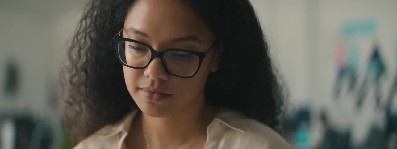 Closeup of the face of a young woman with curly hair and glasses focused on a task