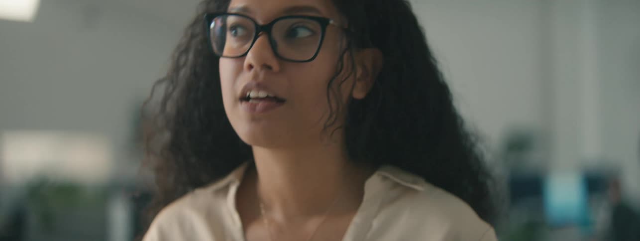 A happy woman with curly hair gestures while talking on a video call in the office