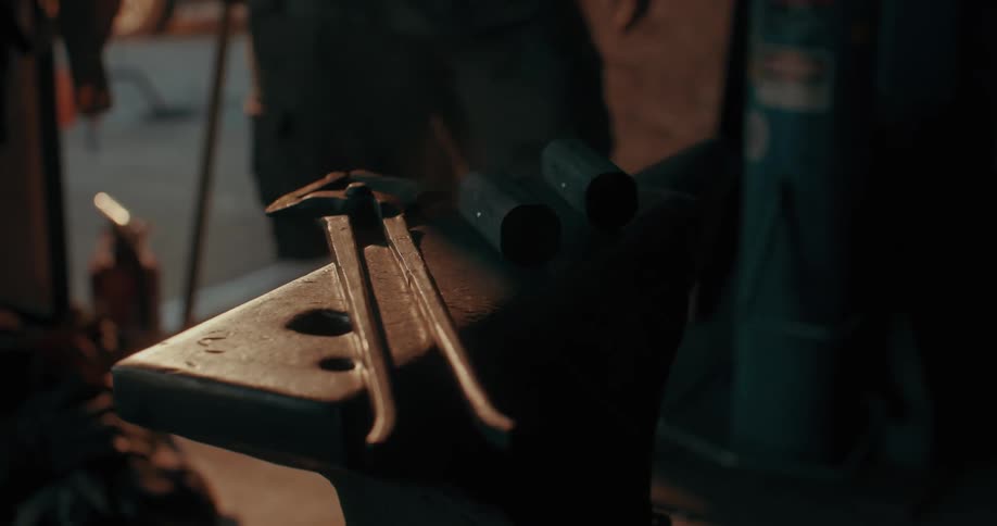 A blacksmith enters a dimly lit workshop where a pair of tongs and metal pieces lie on an anvil