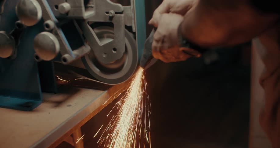 Close up of a mans hands shaping a metal part on a machine