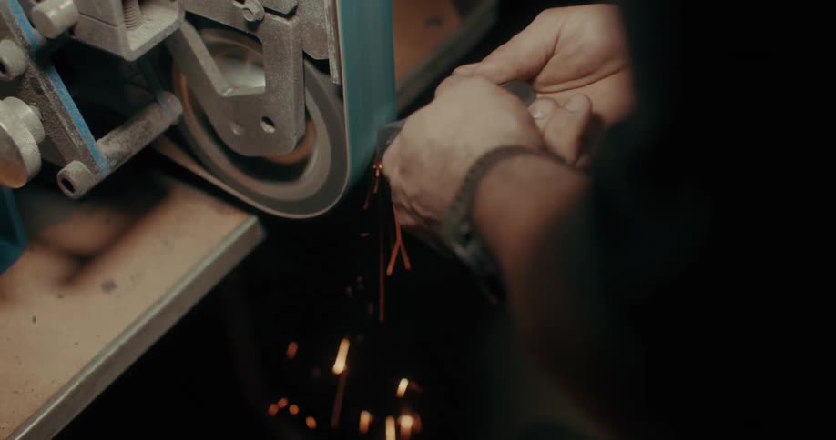 A person works on a metal grinding machine sparks flying as they shape the metal