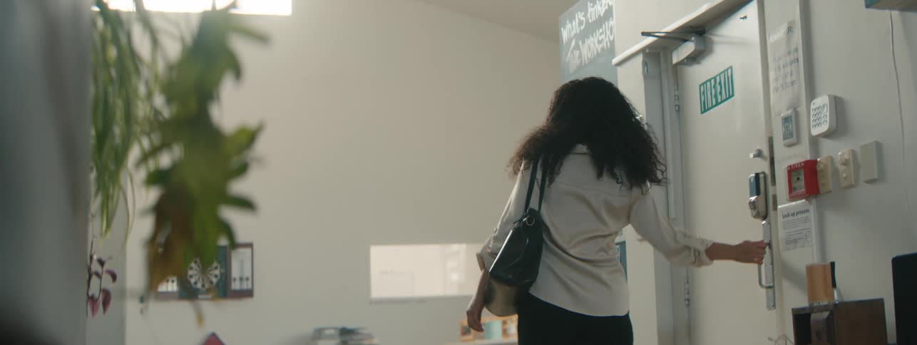 A happy young woman with curly hair enters a modern office