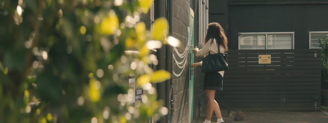 Woman unlocks a door and walks into a building on a sunny summer day
