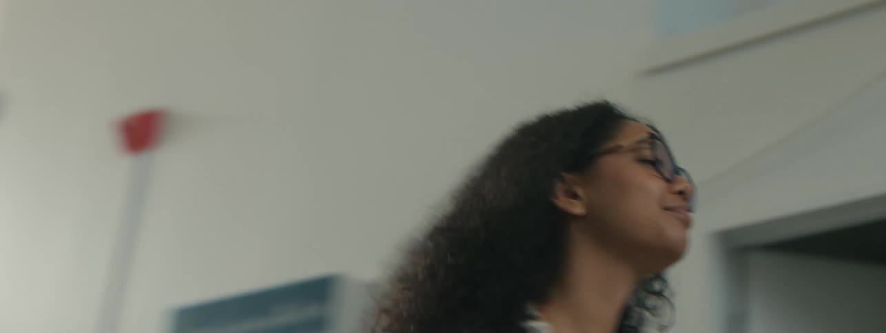 A young woman with curly hair walks through a modern office