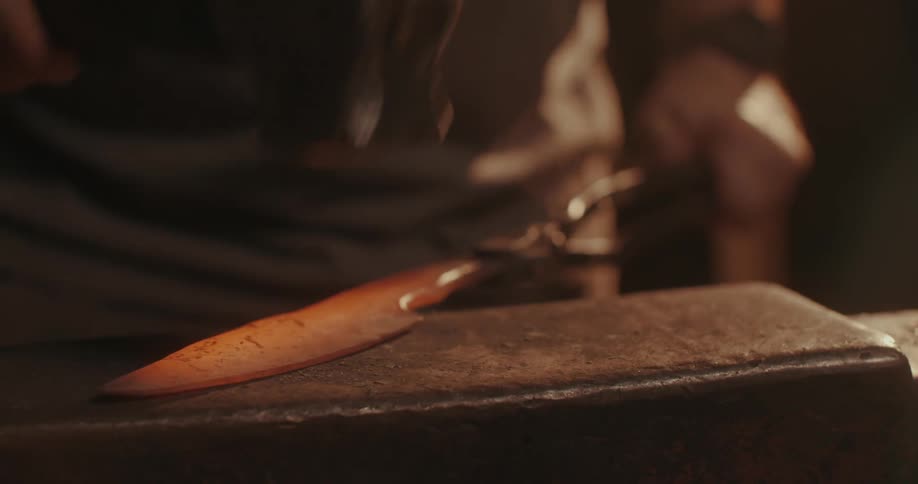 Hand with a hammer forging a heated metal and shaping a knife