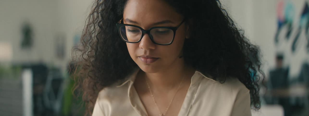 Closeup of the face of a young woman with curly hair and glasses focused on a task