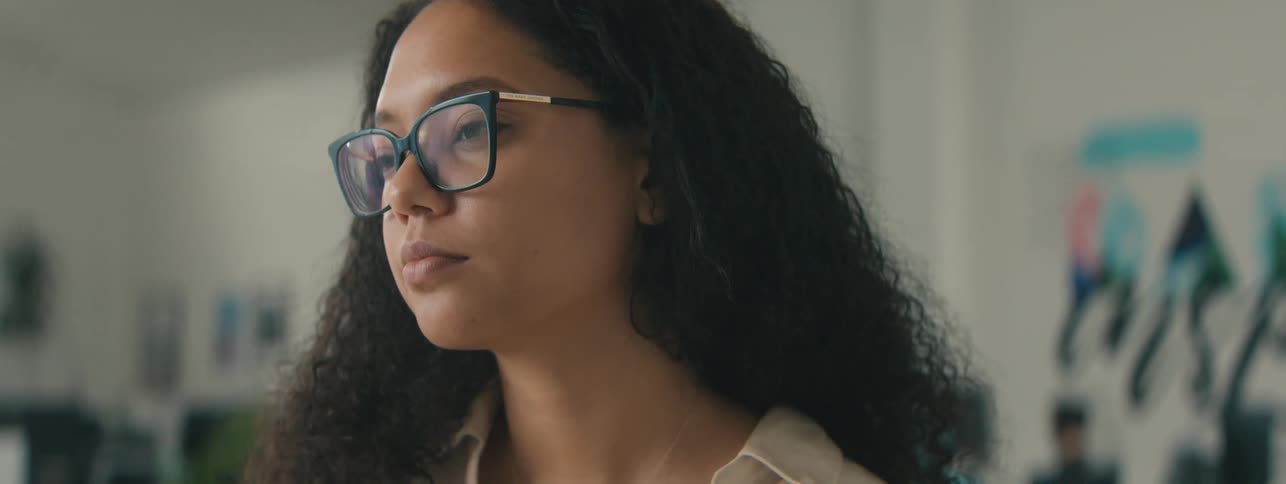 Closeup of the face of a young woman with curly hair and glasses focused on a task