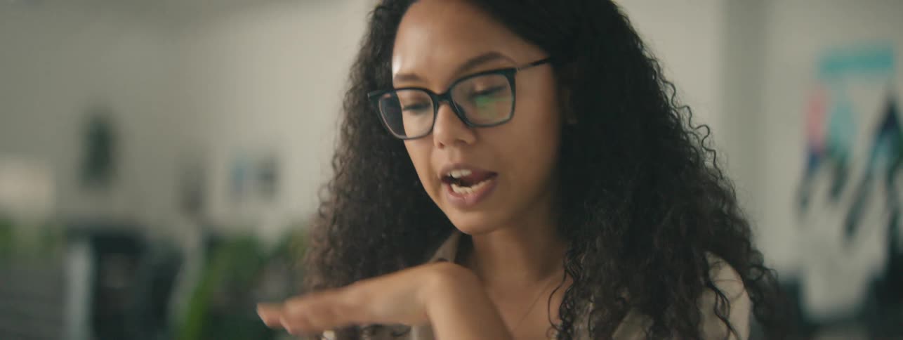 A happy woman with curly hair gestures while talking on a video call in the office