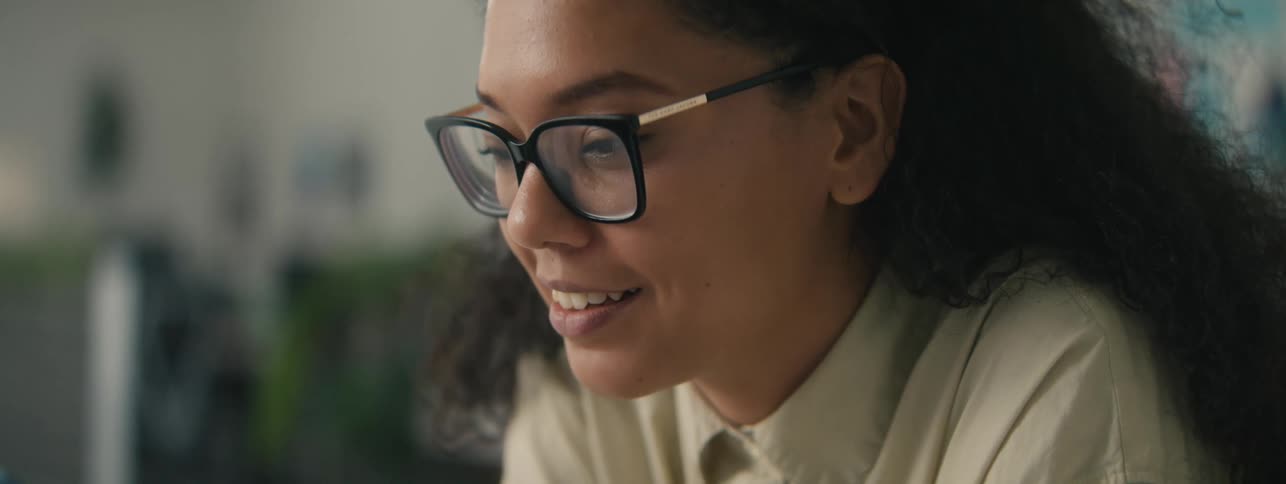 Closeup of the face of a young woman with curly hair and glasses looking at her phone