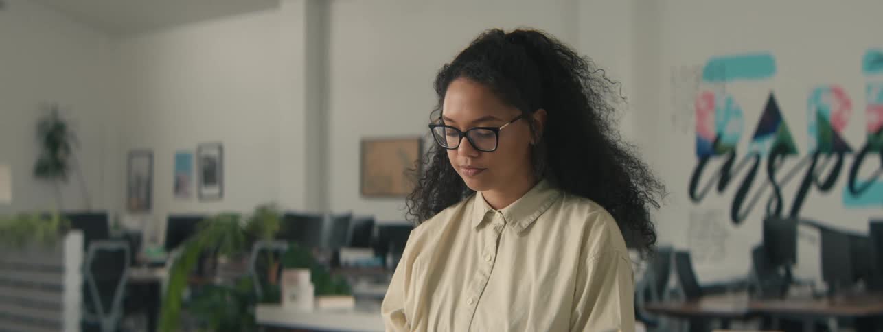 A young woman with curly hair sits down and prepares to work in the office