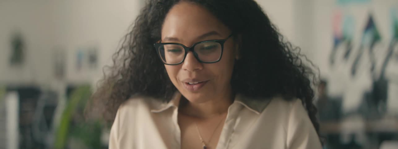 Woman with curly hair and glasses talking cheerfully in an office environment