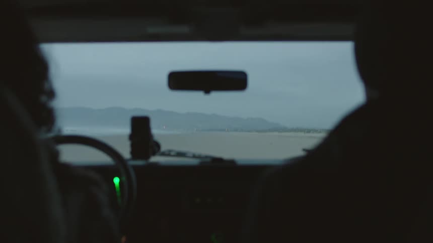 Two people driving towards the mountains on a cloudy day