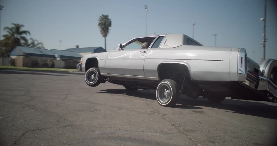 A lowrider car performs a wheelie in a parking lot showcasing its hydraulic suspension system