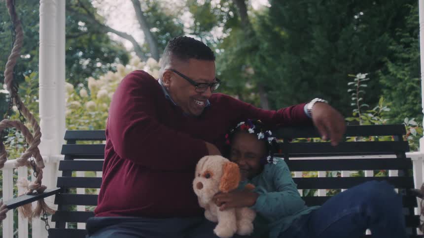 Father playing with his daughter while both are sitting on a bench next to a house