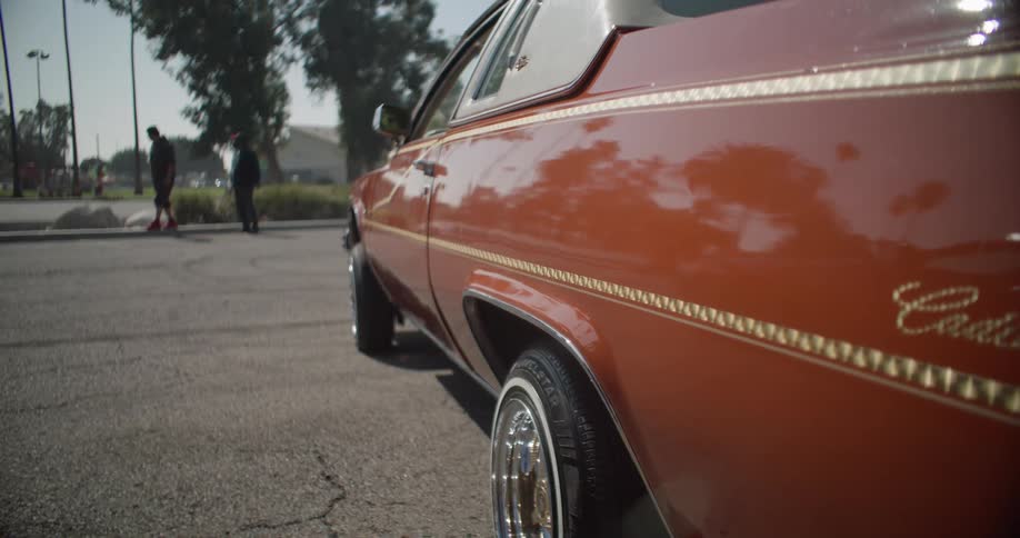 A classic car parked on a street with people standing in the background