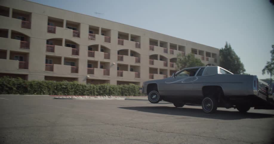 A lowrider car performs a wheelie in a parking lot