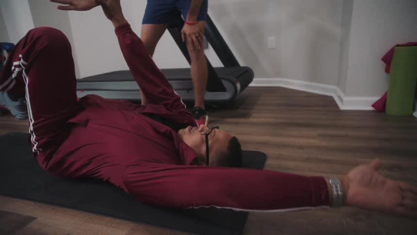 Man lying on a yoga mat doing stretching with the help of another person