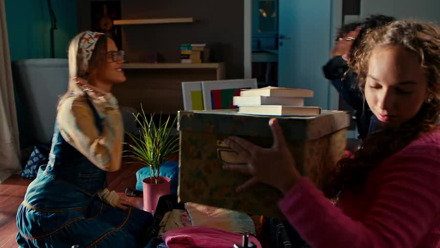 Three friends in a room clapping and packing a suitcase