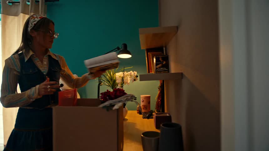A woman takes selfies in the bathroom while another organizes books on a bookshelf