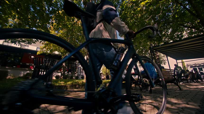 College students outside the college talking and sitting and one of them walking with a bicycle at his side