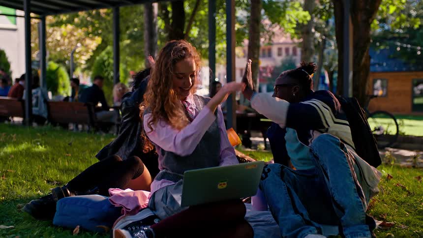 Women sitting on the grass and a man coming to sit together and greet each other while in an academic setting