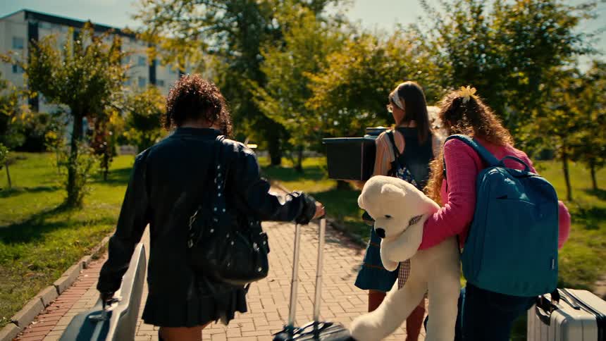 A group of happy friends arrives at a university campus carrying personal belongings