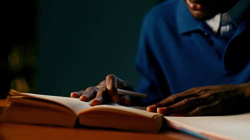 A person sits on a luxurious chair studying a book and taking notes