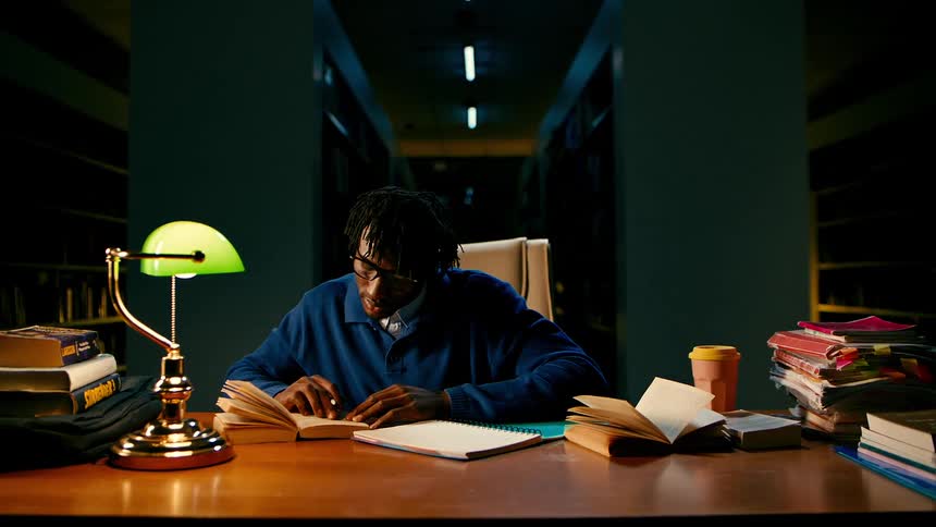 A man is studying and writing in the library