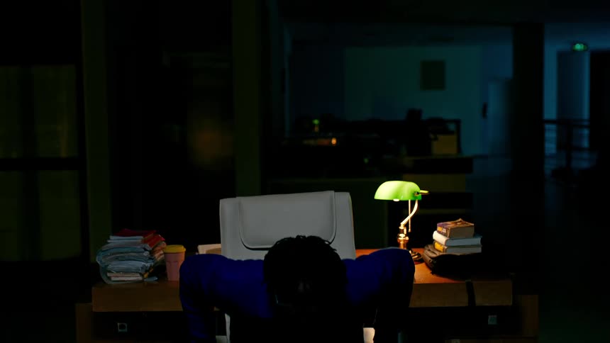Man student sitting on a chair and standing up while being late at night in a library