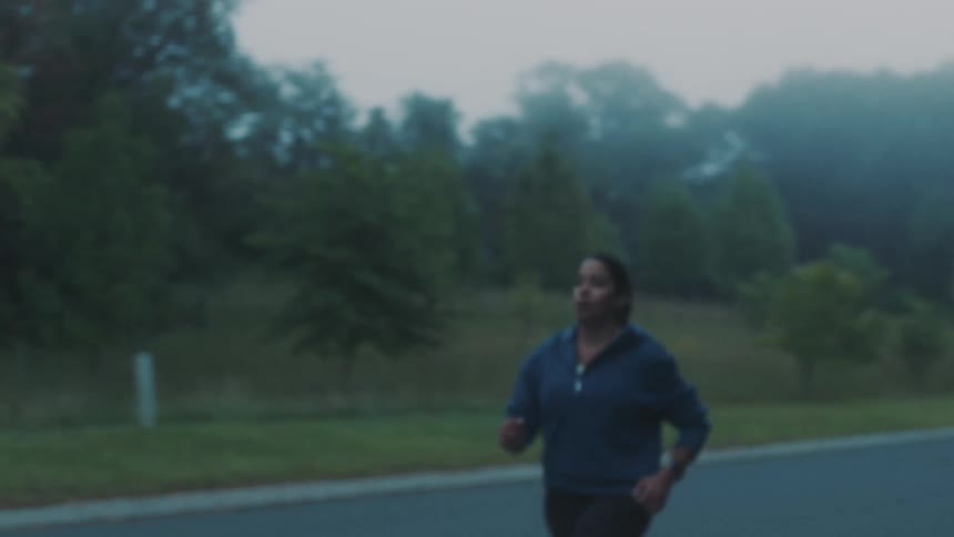 A woman runs down a paved road early in the morning with fog in the background
