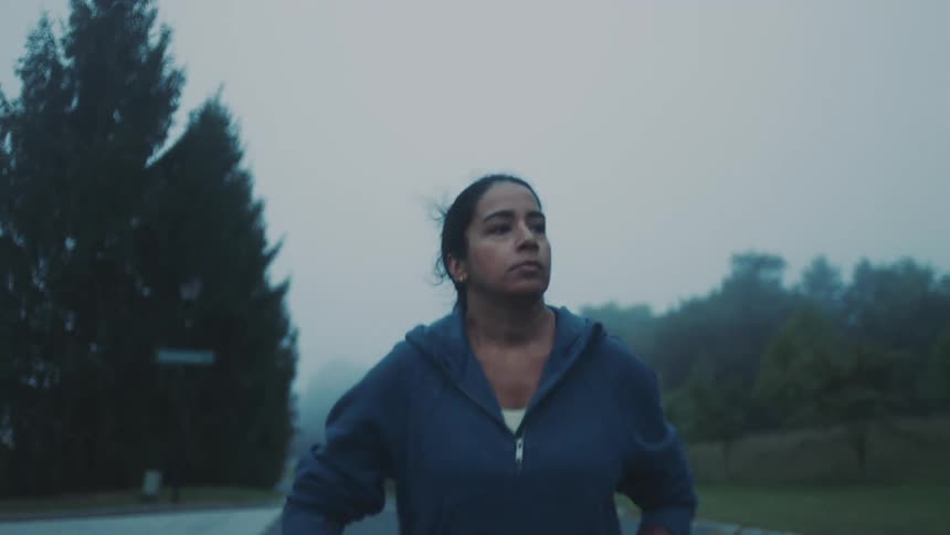 A woman jogging on an empty street surrounded by trees on a misty morning
