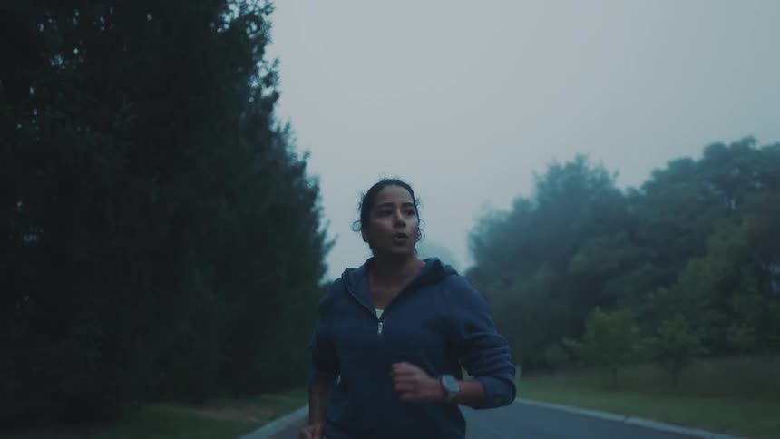 A woman jogs on a road in the morning with fog hanging over the trees