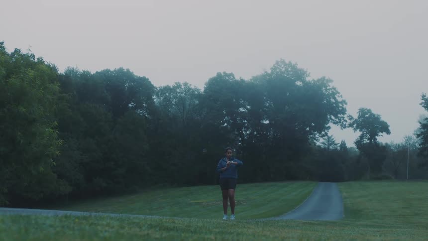 Female jogger sets her watch before starting her run on a path through the park on a misty day