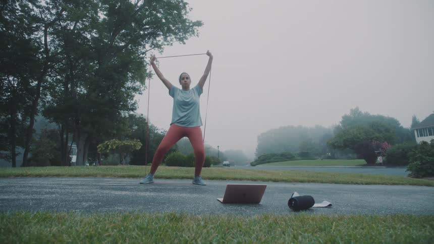 Woman using a rubber band and stretching her body while standing outside in a residential neighborhood