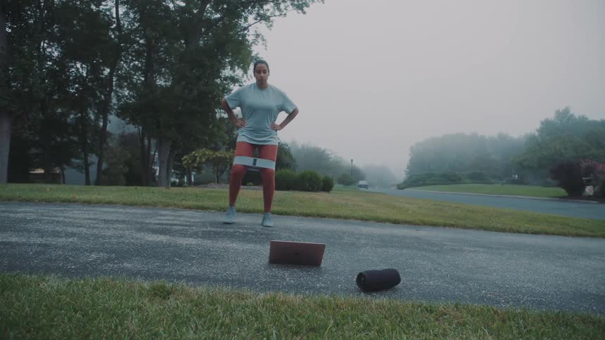 A young woman uses a leg band to exercise outdoors on a cloudy summer day
