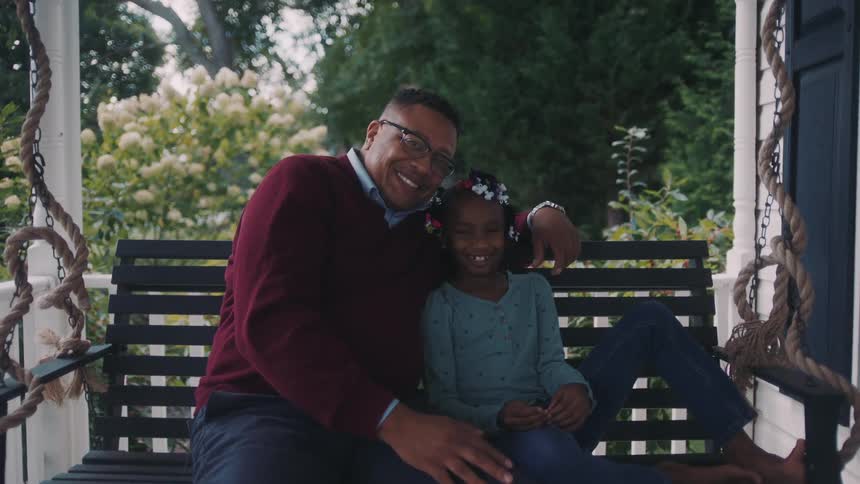 Cheerful father and daughter sitting on a porch swing