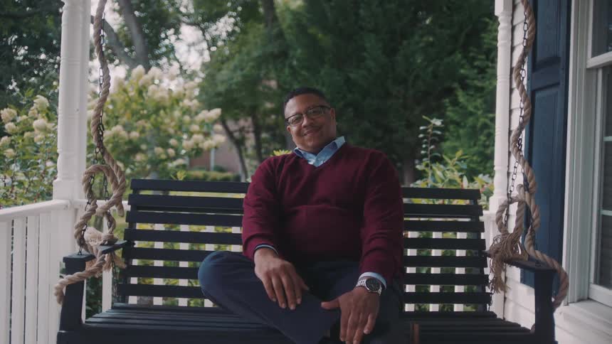 Smiling man sitting on a bench in an outdoor area of a house with trees in the background