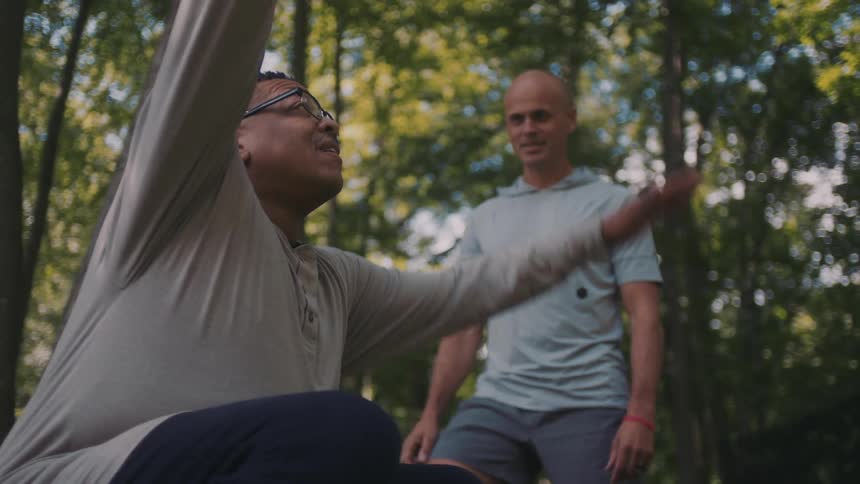 Man crouched down raising his hands and standing up and another man next to him following suit