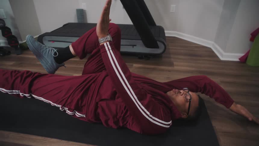 A man in red sports overalls stretches on a mat near a walking machine at home