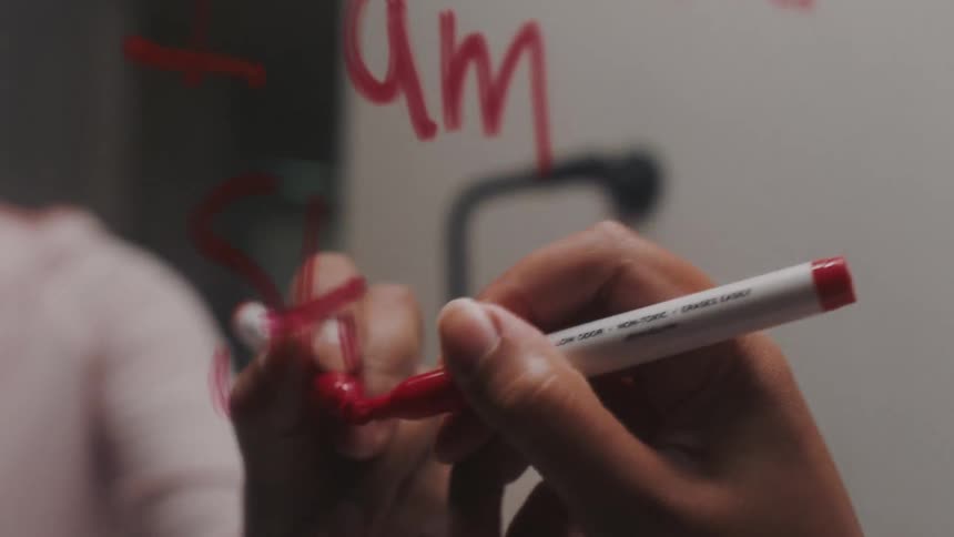 Close up of a womans hand holding a red pen and writing on the mirror