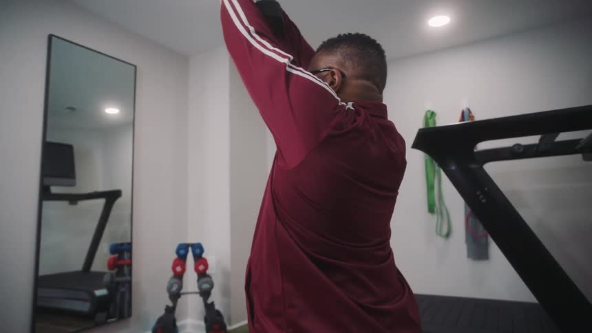 Man in a room facing the mirror and lifting a dumbbell with his arms