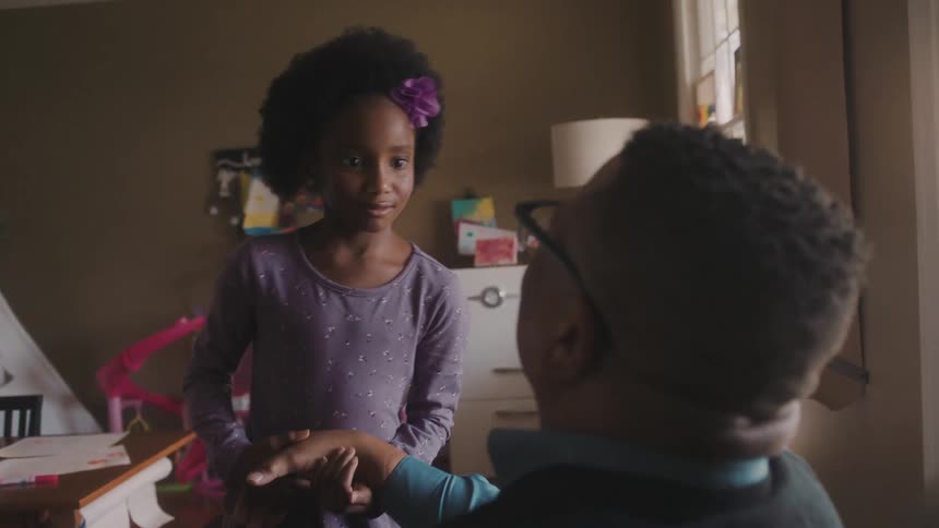 A girl in a purple dress playing with her dad in the bedroom